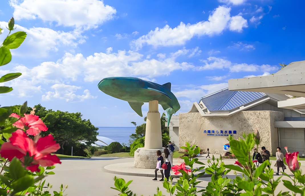 Entrance to Okinawa Churaumi Aquarium with whale shark statue and visitors.