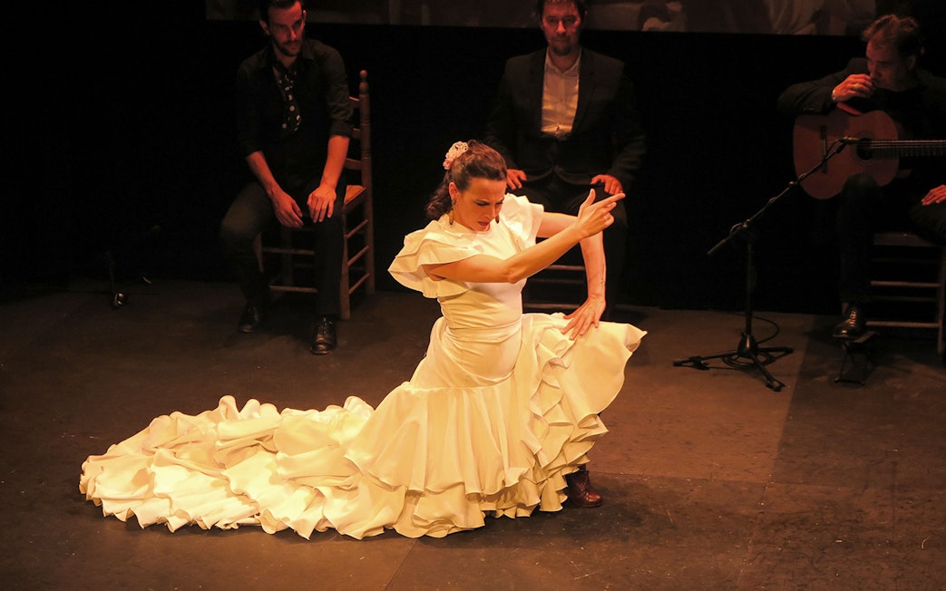 Flamenco dancer performing at Triana Theater with musicians in the background.