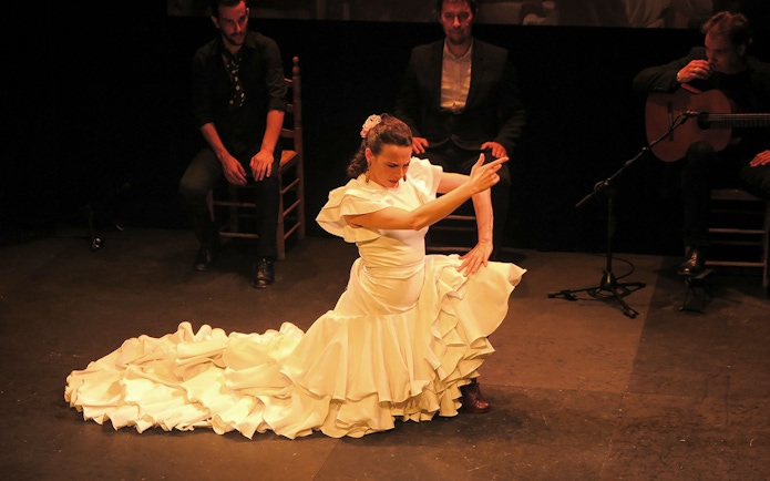 Flamenco dancer performing at Triana Theater with musicians in the background.