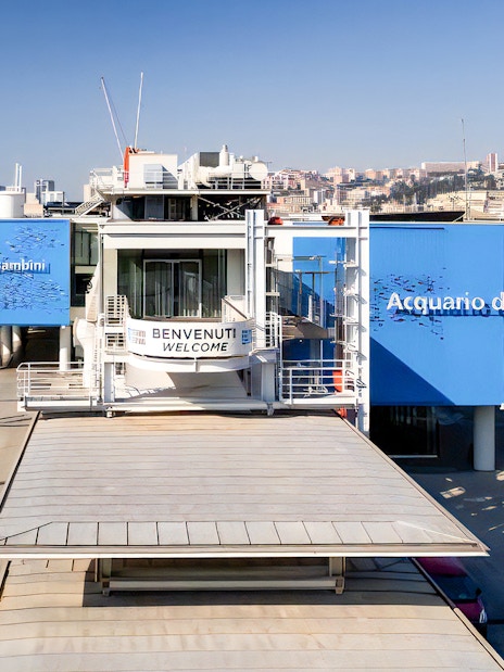 Exterior view of Aquarium of Genoa and City of Kids entrance, with nearby harbor and cityscape.