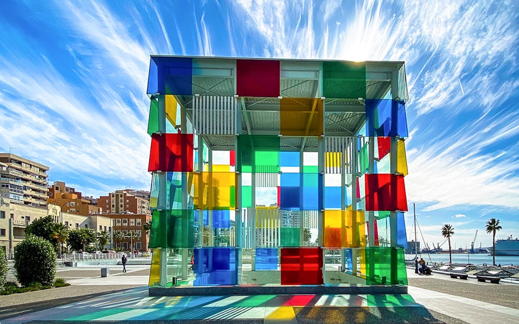 Colorful glass cube structure at Centre Pompidou Malaga with cityscape and sky in the background.