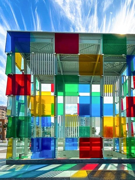 Colorful glass cube structure at Centre Pompidou Malaga with cityscape and sky in the background.