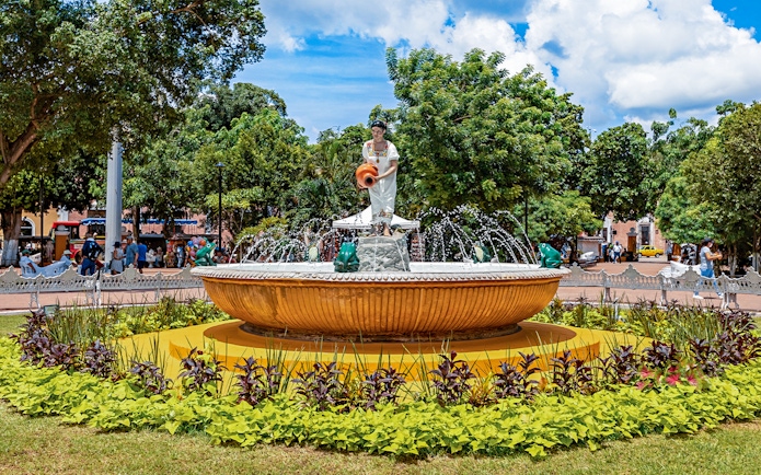 Fountain with statue in Valladolid's central park, Mexico, surrounded by greenery.