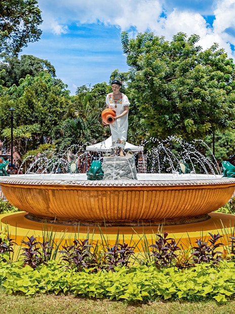Fountain with statue in Valladolid's central park, Mexico, surrounded by greenery.
