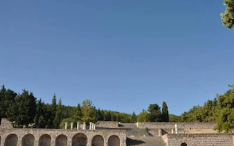 Ancient stone arches and steps at Asclepieion, Kos, surrounded by trees under a clear sky.