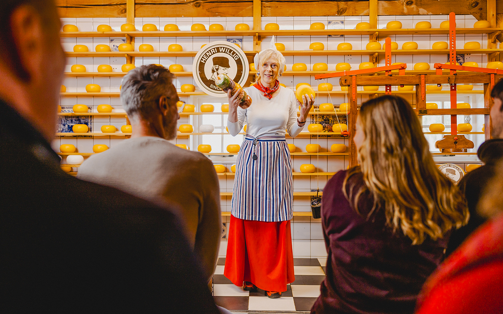 Cheese tasting demonstration at Zaanse Schans with shelves of cheese wheels.