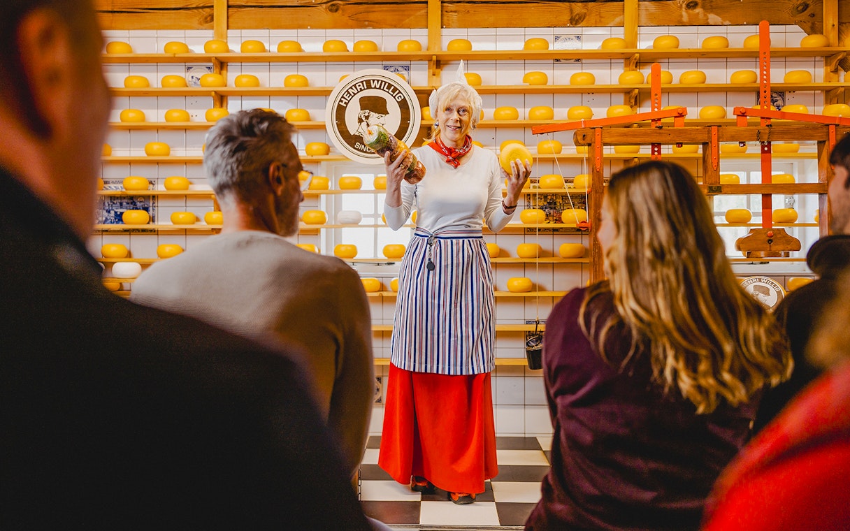 Cheese tasting demonstration at Zaanse Schans with shelves of cheese wheels.