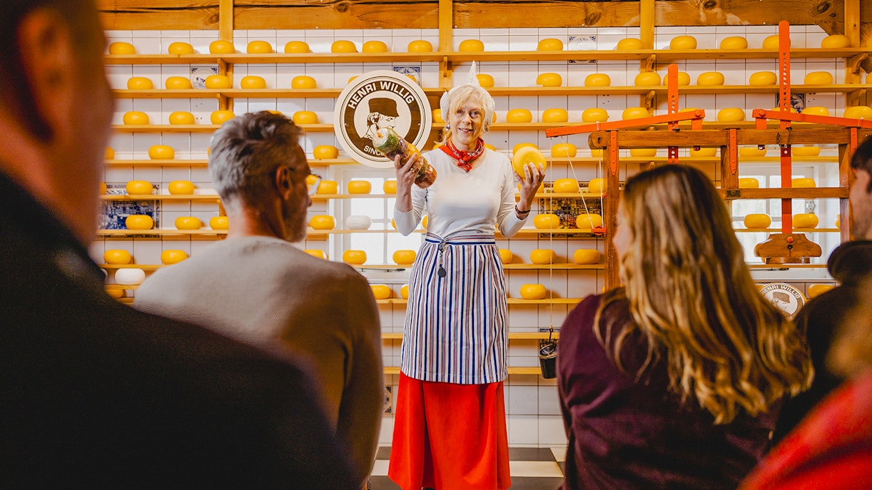 Cheese tasting demonstration at Zaanse Schans with shelves of cheese wheels.