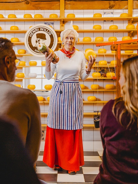 Cheese tasting demonstration at Zaanse Schans with shelves of cheese wheels.