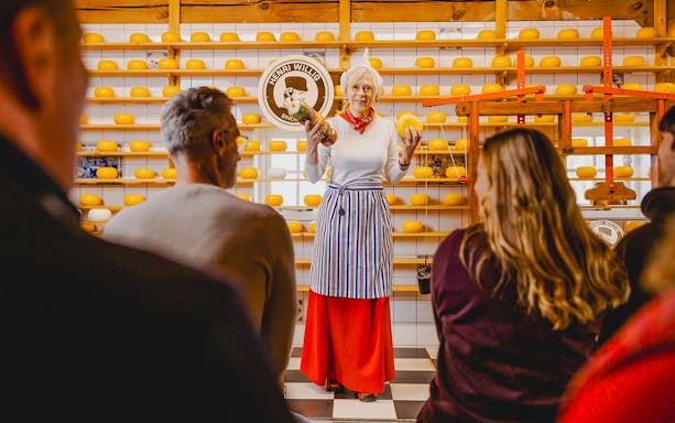 Cheese tasting demonstration at Zaanse Schans with shelves of cheese wheels.