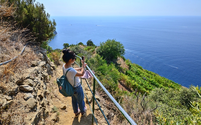 Traveler photographing the sea view along a hiking trail in Cinque Terre, Italy.