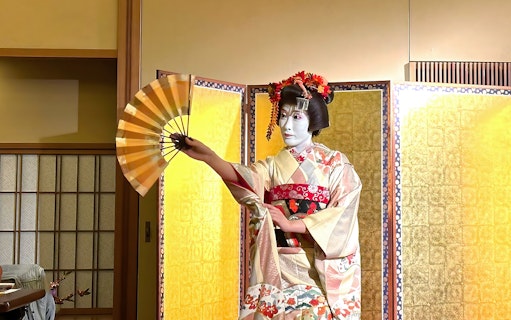 Geisha in traditional kimono performing with a fan at a dinner event in Japan.