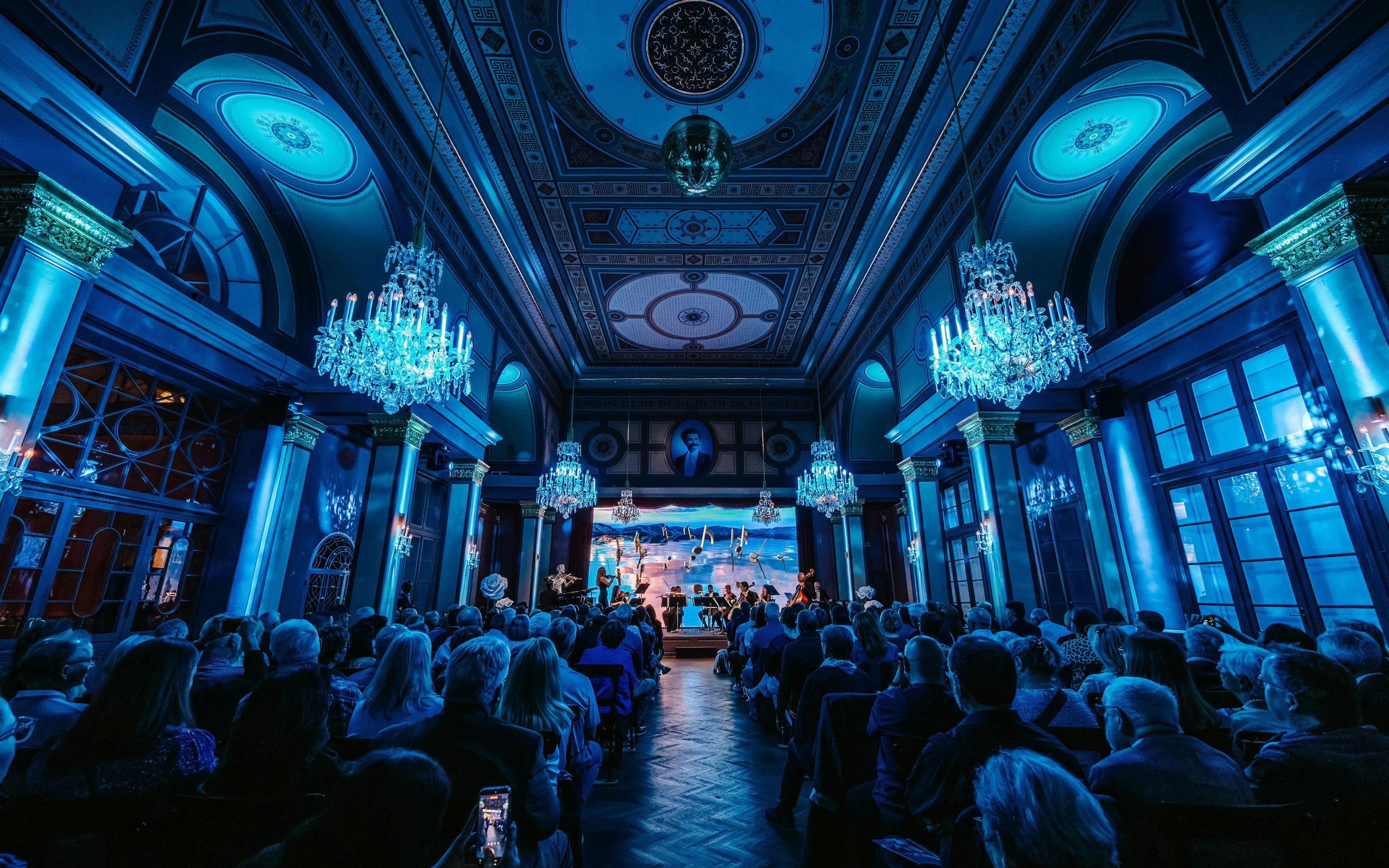 Classical concert in Vienna hall with chandeliers and audience.