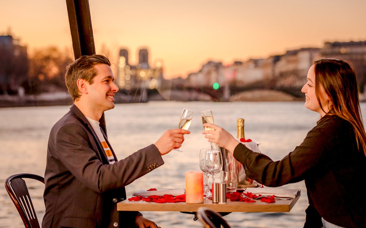 Couple toasting with champagne on Seine River cruise at sunset in Paris.