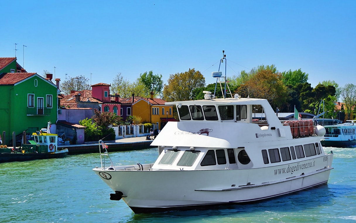 Tour boat cruising past colorful houses on Burano Island, Italy.
