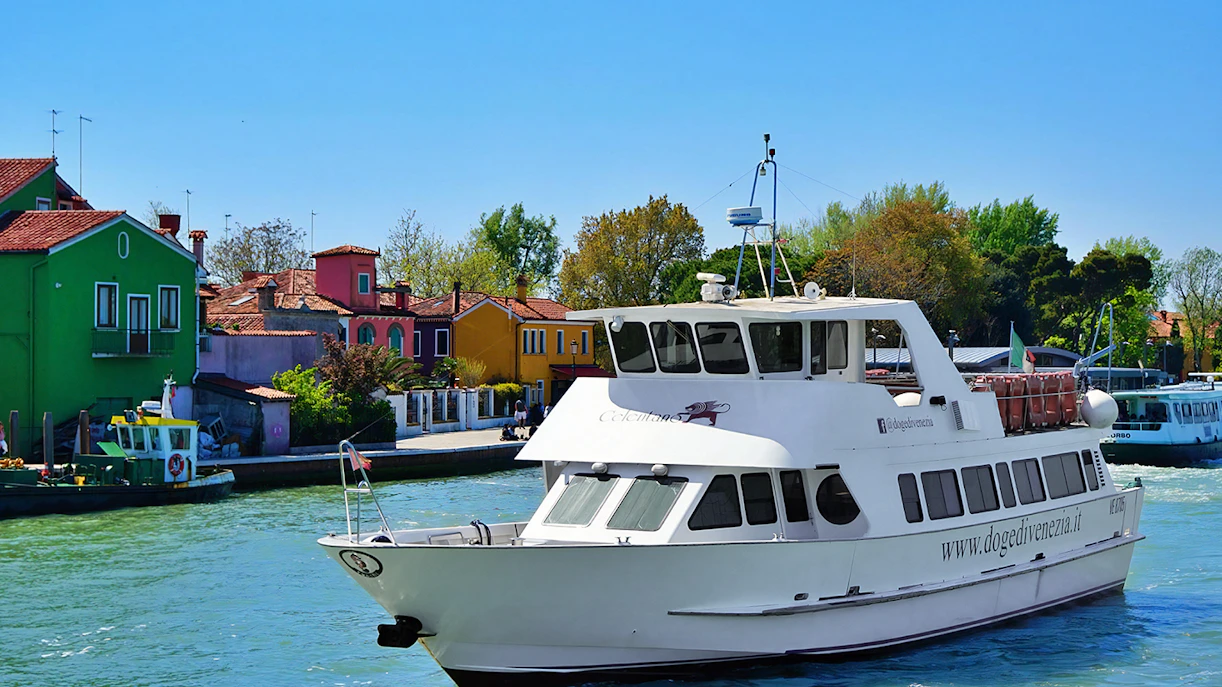 Tour boat cruising past colorful houses on Burano Island, Italy.