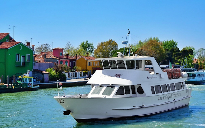 Tour boat cruising past colorful houses on Burano Island, Italy.