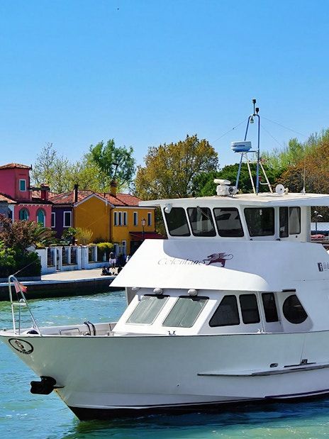 Tour boat cruising past colorful houses on Burano Island, Italy.