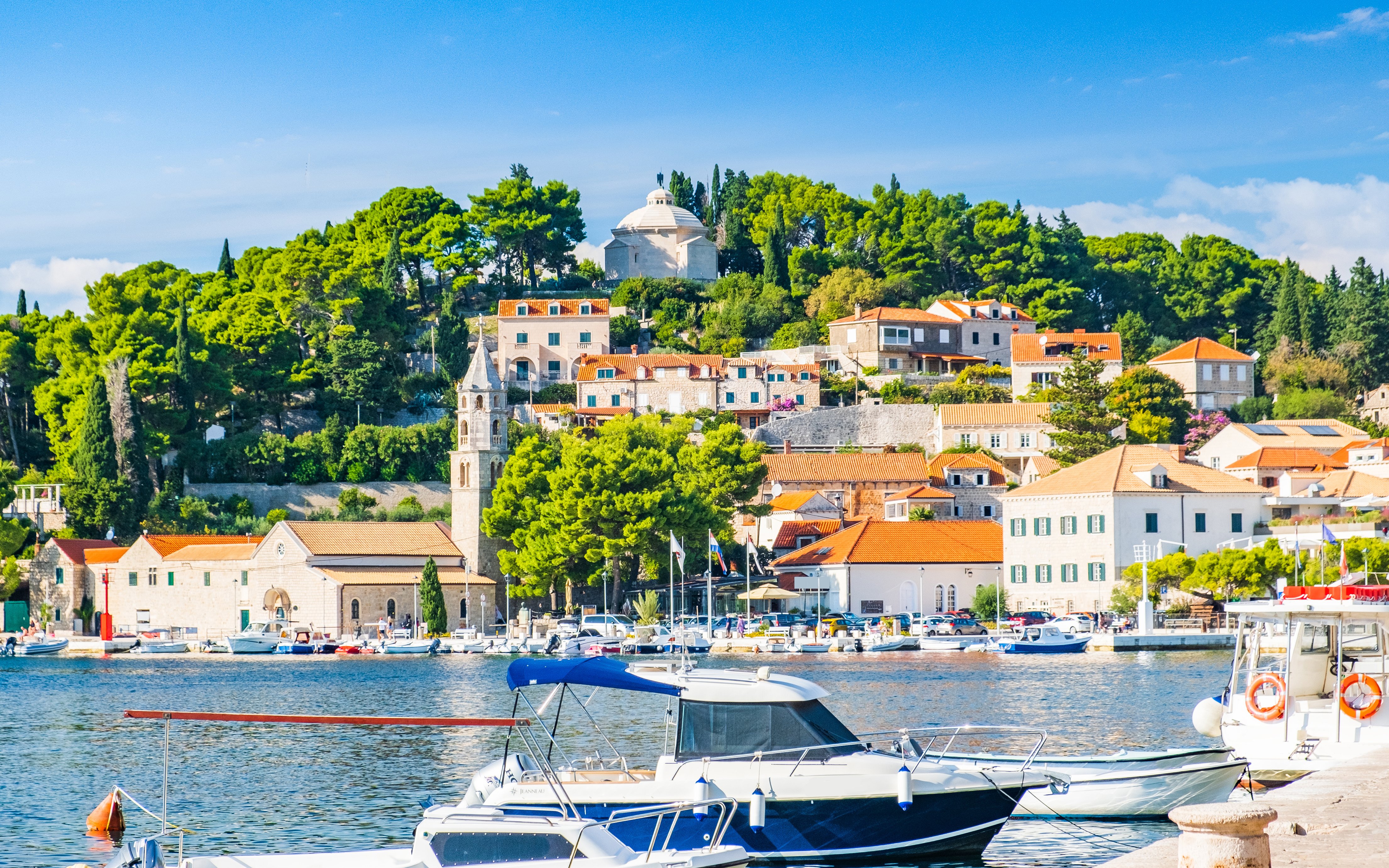 Boats docked in the harbor of Cavtat, south Dalmatia, Croatia, with historic buildings and lush greenery.