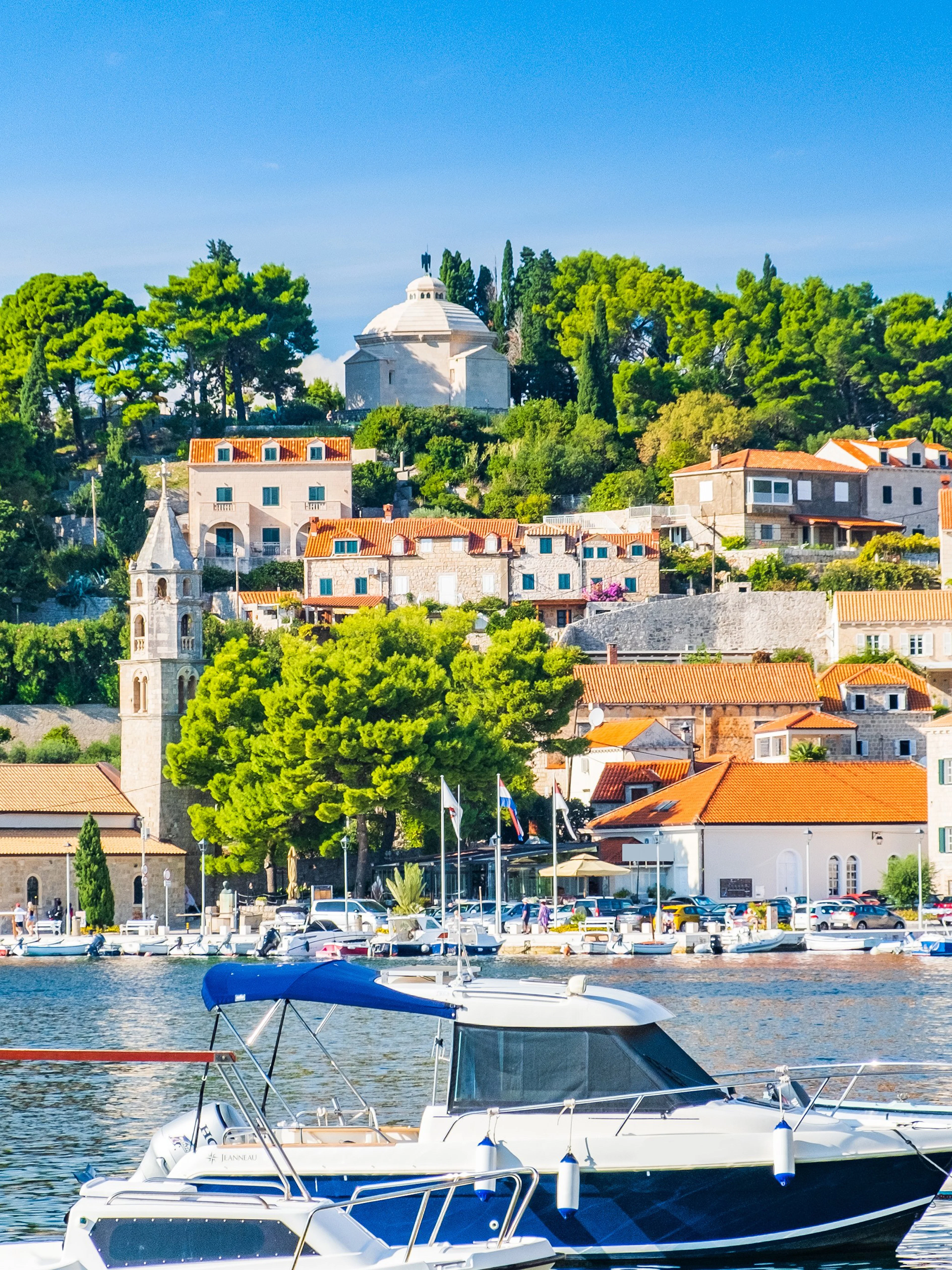 Boats docked in the harbor of Cavtat, south Dalmatia, Croatia, with historic buildings and lush greenery.