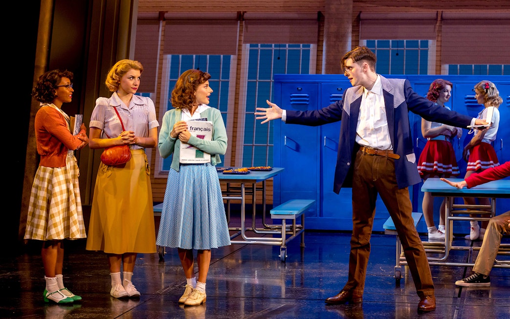 Stage scene from "Back to the Future" musical with actors in 1950s attire.