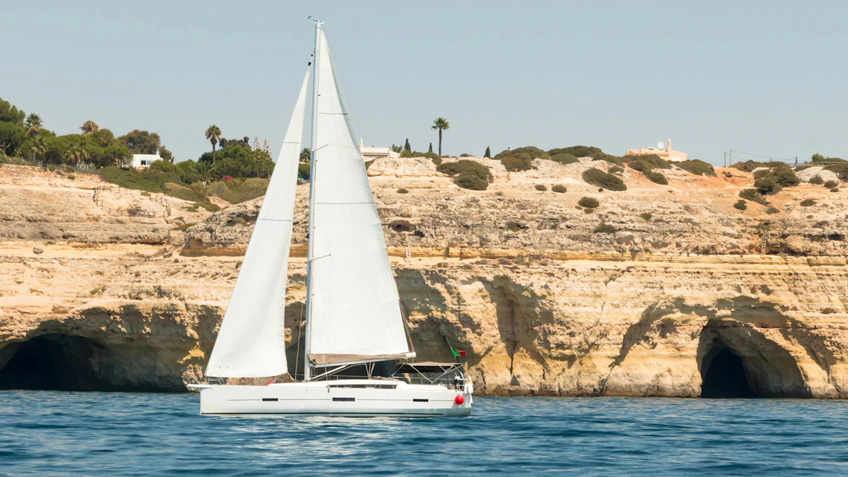 Sailboat near cliffs and caves in Algarve, southern Portugal.