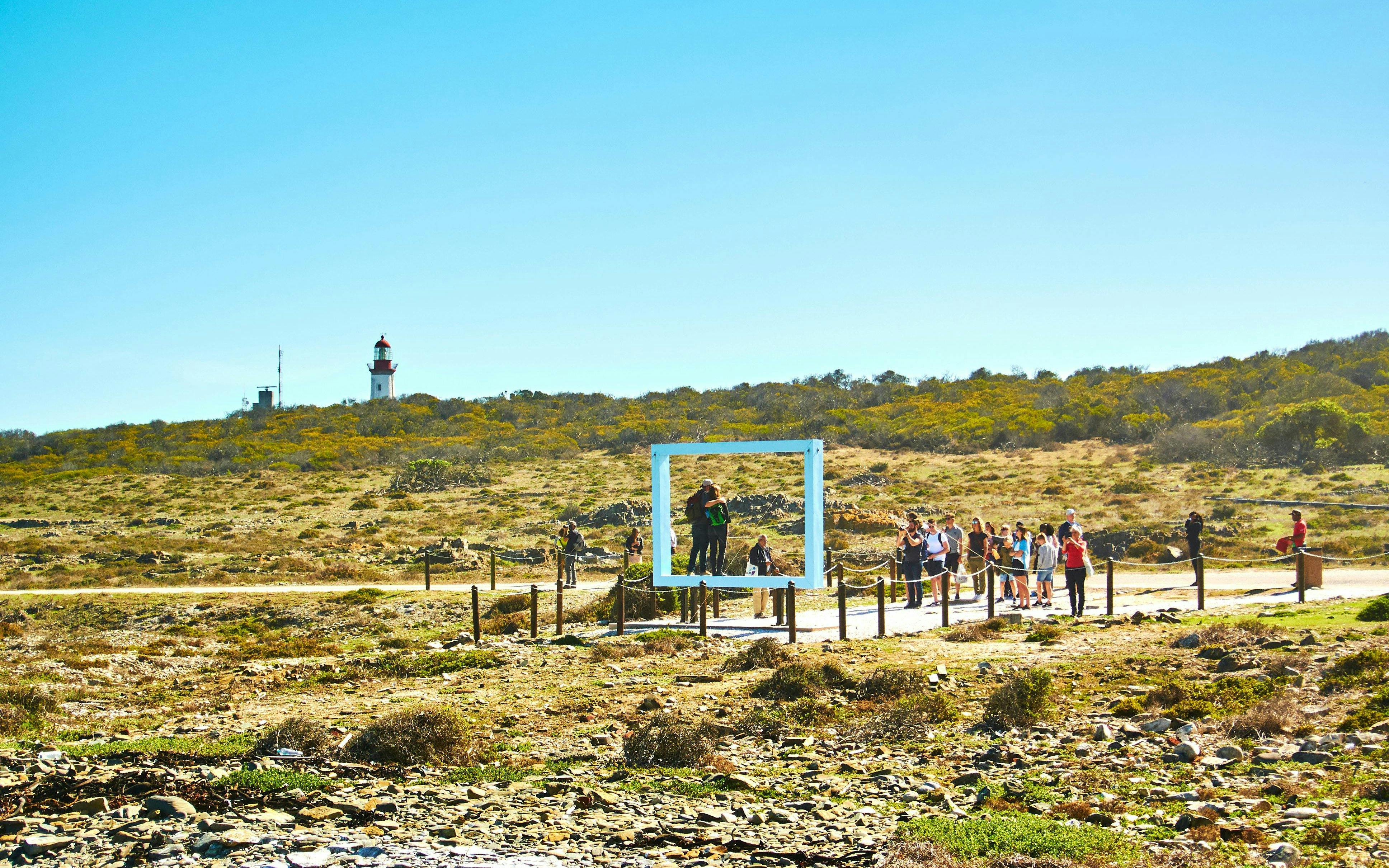 Tourists exploring Robben Island with a lighthouse in the background.