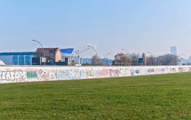 Graffiti-covered Berlin Wall section in Kreuzberg, Germany, with cityscape in background.