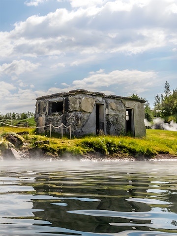 Old stone building by the Secret Lagoon with steam rising from the water, Iceland.