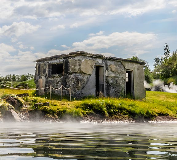 Old stone building by the Secret Lagoon with steam rising from the water, Iceland.