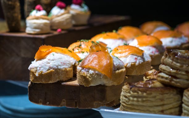 Salmon and crayfish tapas on bread slices, garnished with herbs.