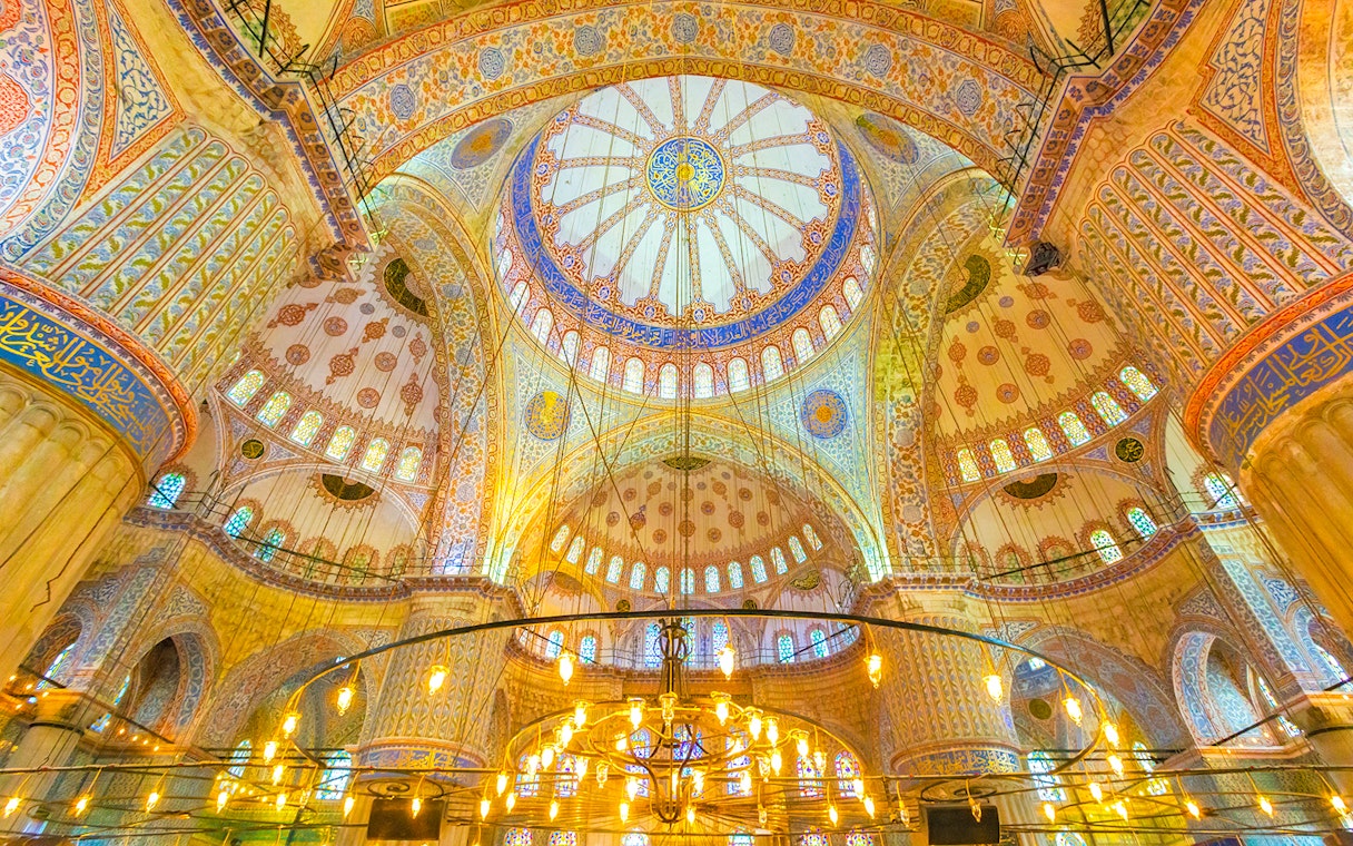 Interior of the Blue Mosque in Istanbul, showcasing intricate domed ceiling and ornate designs.