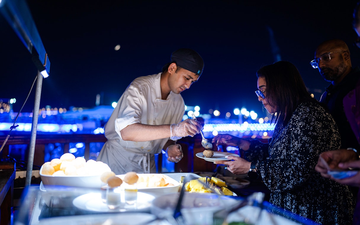 Chef serving Indian dinner on Dubai Marina luxury dhow cruise.