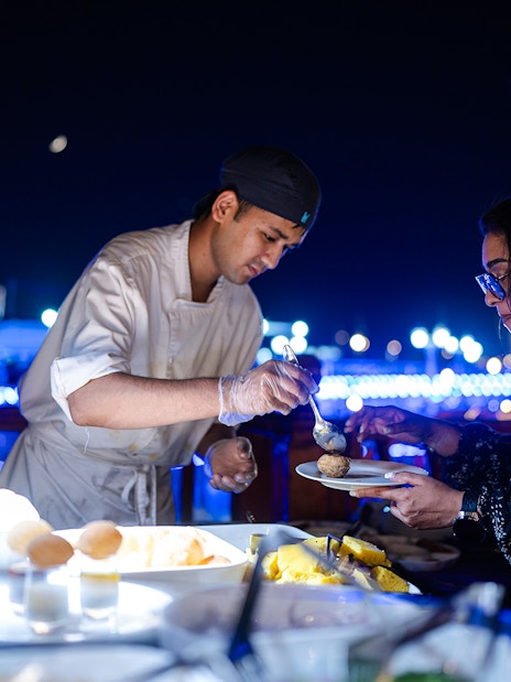 Chef serving Indian dinner on Dubai Marina luxury dhow cruise.