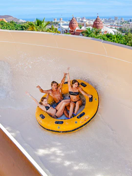 Group enjoying a water ride at Siam Park, Tenerife, with cityscape in the background.