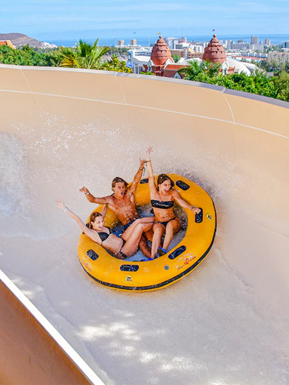 Group enjoying a water ride at Siam Park, Tenerife, with cityscape in the background.