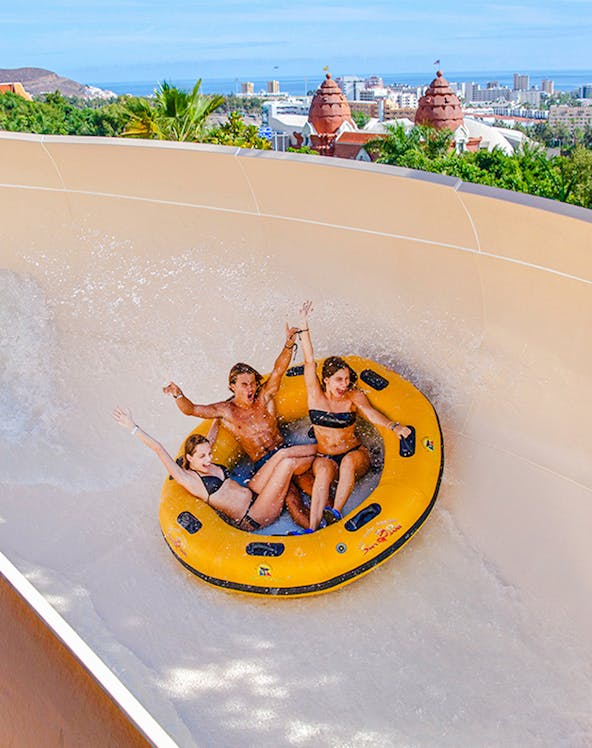 Group enjoying a water ride at Siam Park, Tenerife, with cityscape in the background.