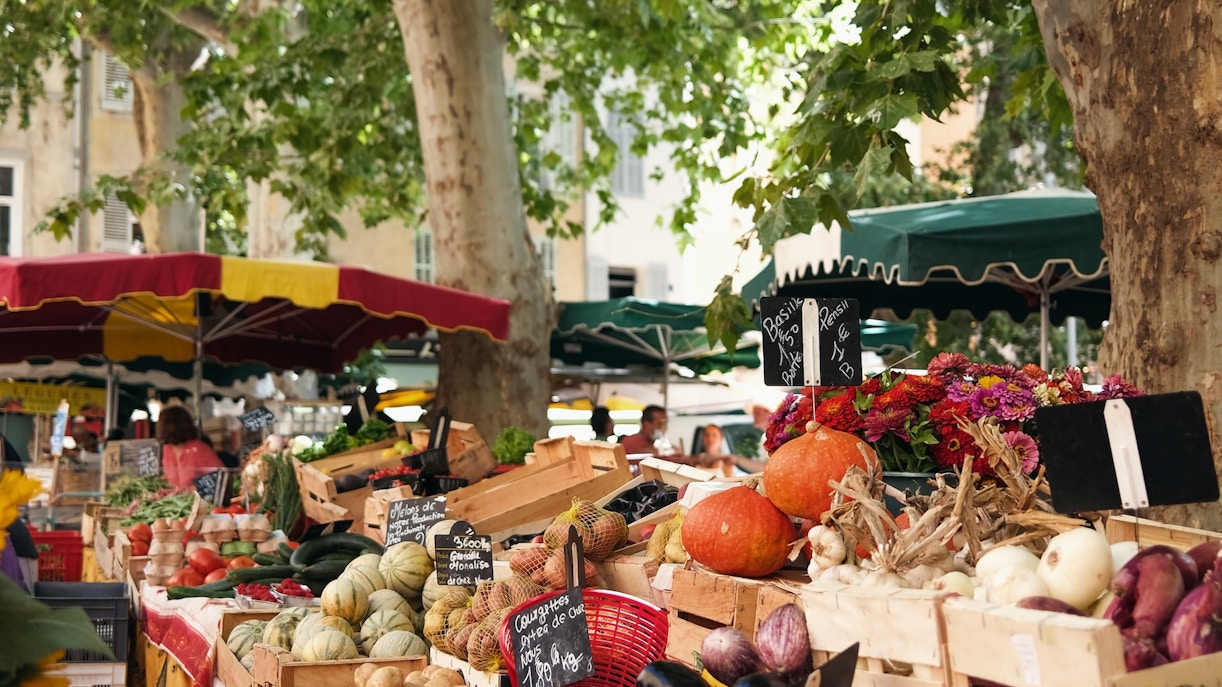 Provence market with fresh vegetables and fruits under trees.