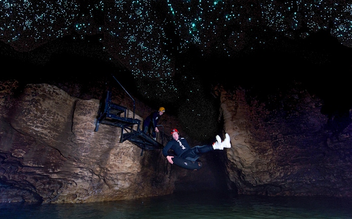 Person black water rafting under glowworms in Waitomo cave.