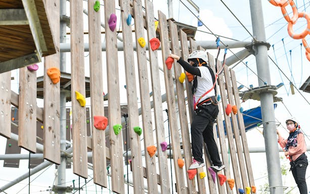 Person climbing a wooden wall with colorful holds at Discovery Park, Gamuda Cove.