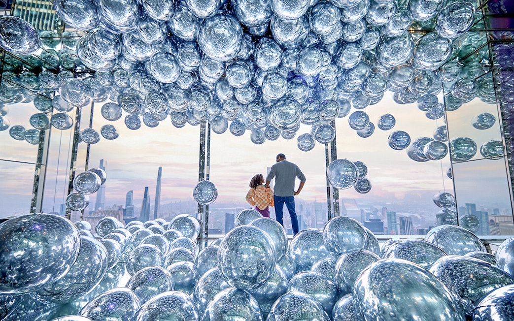 Visitors at SUMMIT One Vanderbilt surrounded by reflective spheres with a cityscape view.
