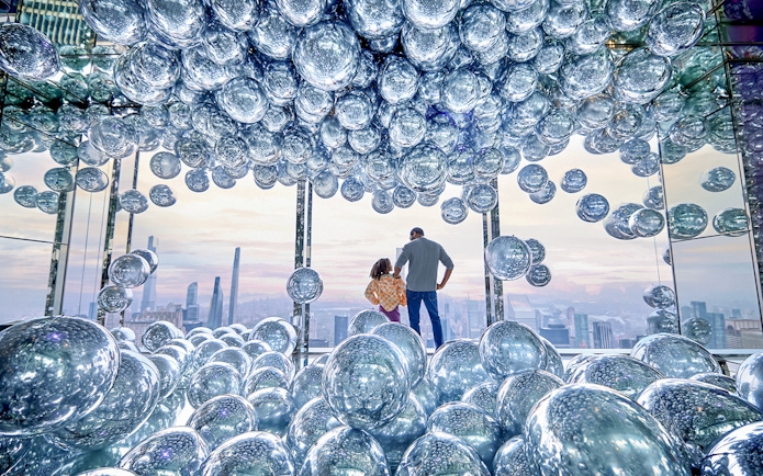 Visitors at SUMMIT One Vanderbilt surrounded by reflective spheres with a cityscape view.