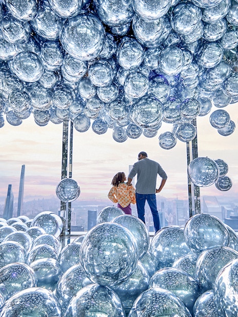 Visitors at SUMMIT One Vanderbilt surrounded by reflective spheres with a cityscape view.
