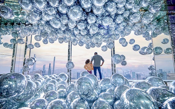 Visitors at SUMMIT One Vanderbilt surrounded by reflective spheres with a cityscape view.