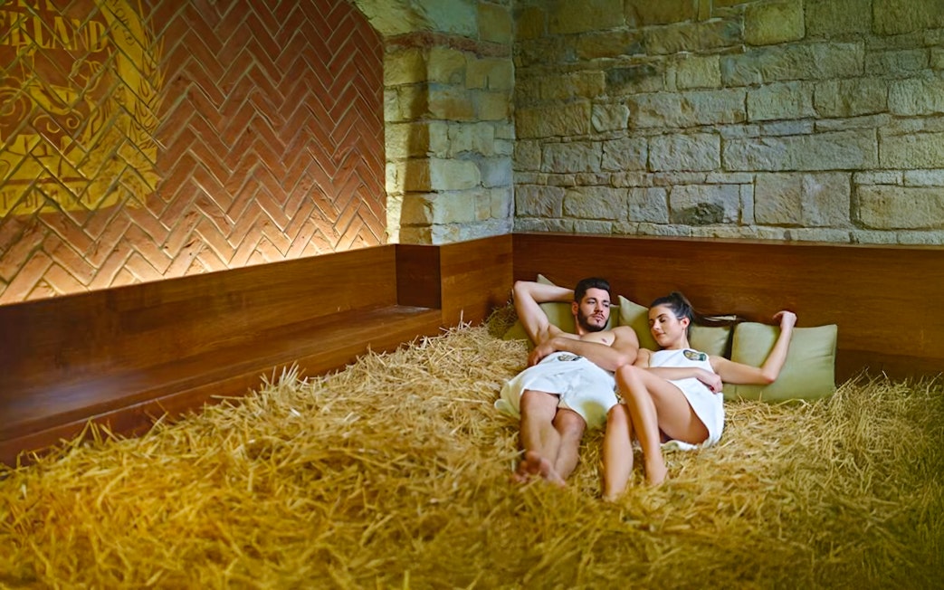 Couple relaxing on hay bed at Prague Spa Beerland with stone walls.