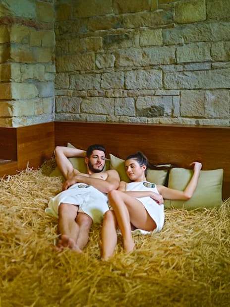 Couple relaxing on hay bed at Prague Spa Beerland with stone walls.
