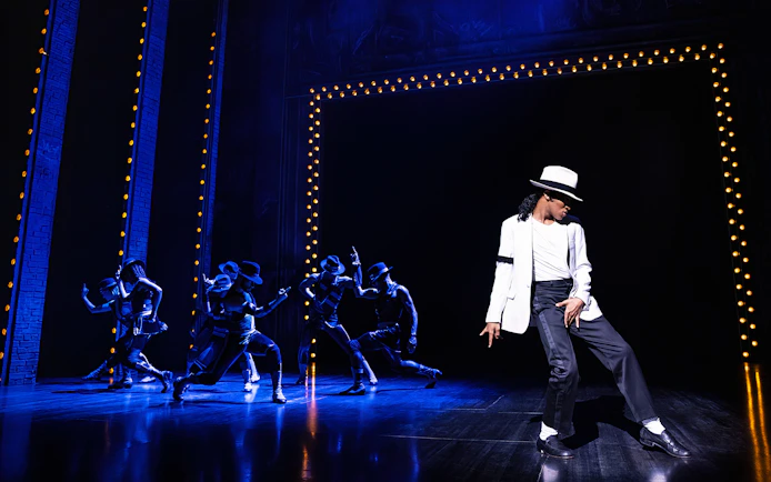 Performer in white suit and hat dancing on stage with backup dancers at MJ Live Tribute Concert.
