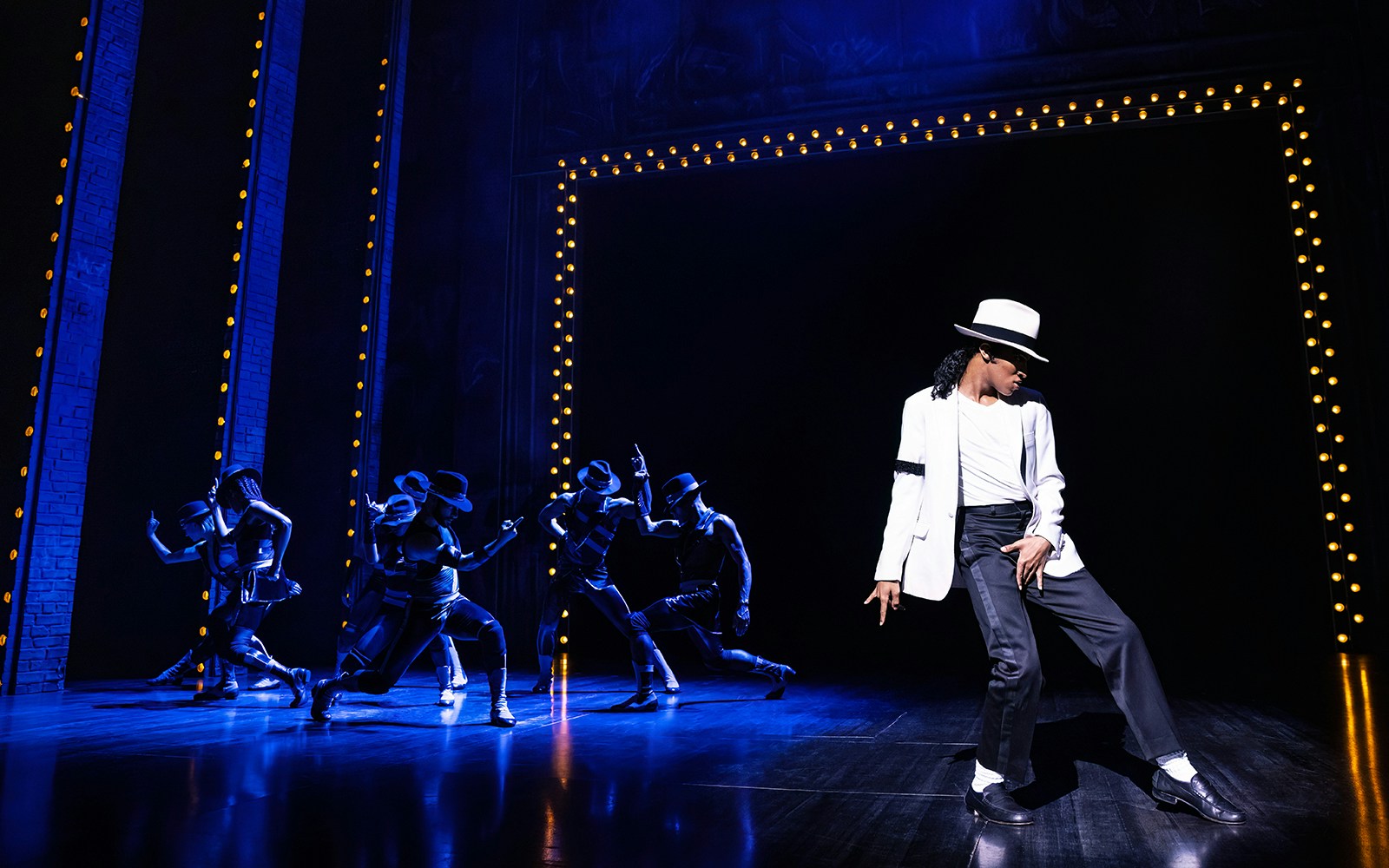 Performer in white suit and hat dancing on stage with backup dancers at MJ Live Tribute Concert.