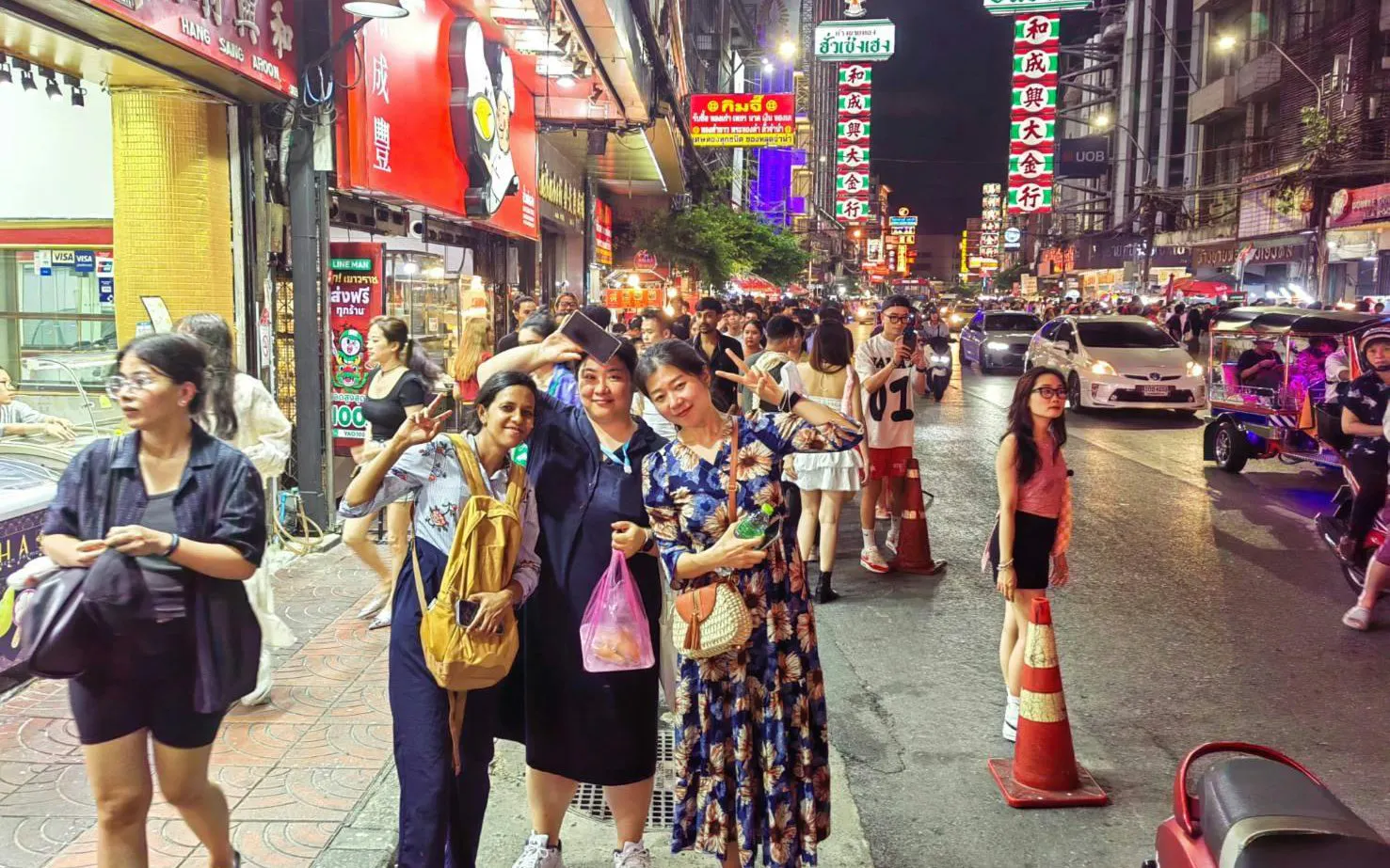Night market street scene in Bangkok with people and tuk tuks.