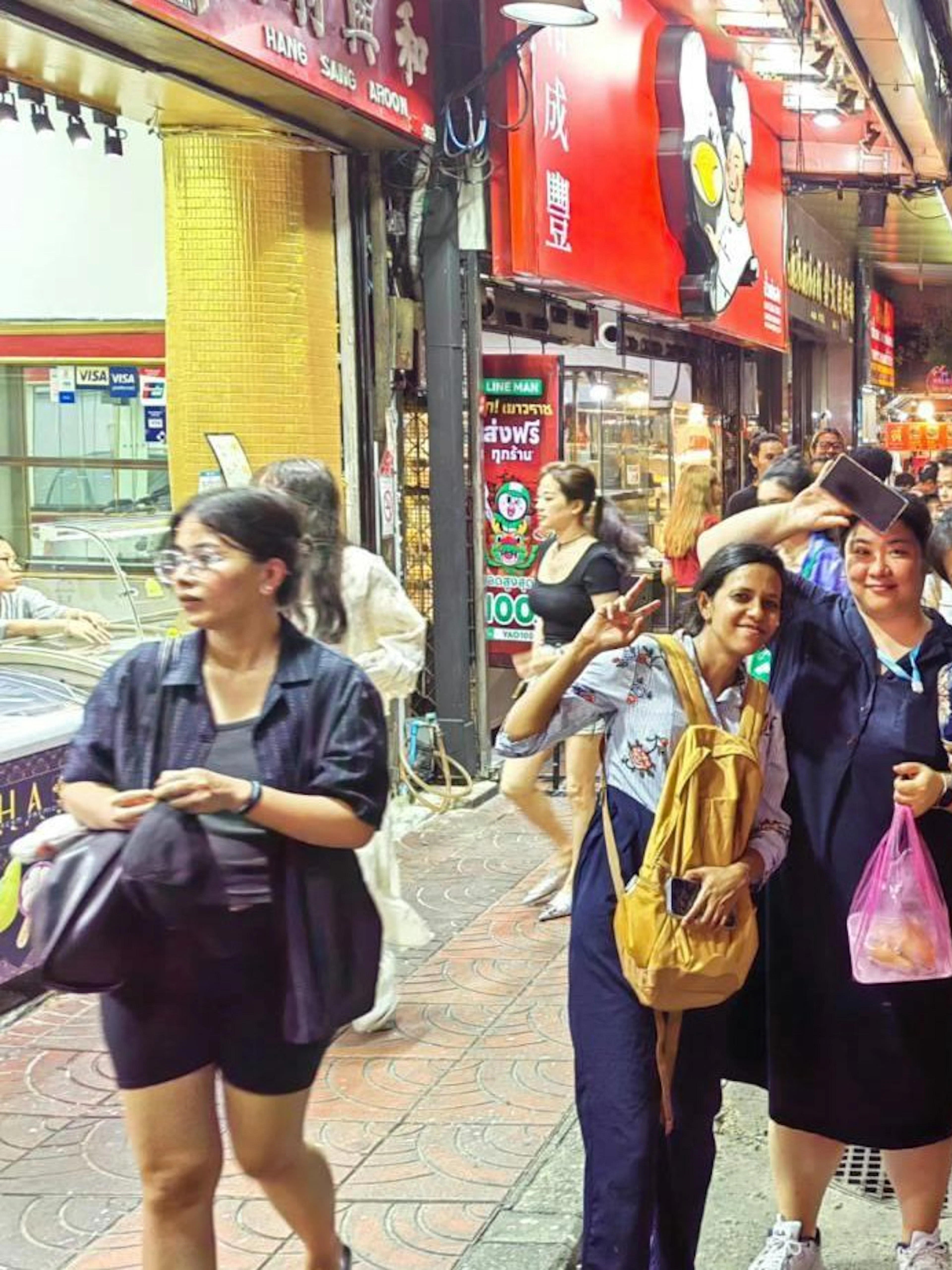 Night market street scene in Bangkok with people and tuk tuks.